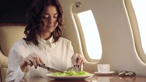smiling businesswoman eating fresh salad while traveling by plane