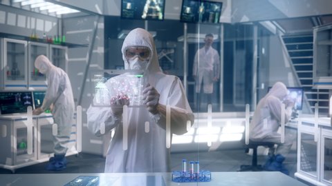 Inside Quarantine Secure High Level Laboratory Scientists in a Coverall Conducting a Research Trying to Make Coronavirus Disease Treatment using Transparent Display Tablets and Modern Technology.