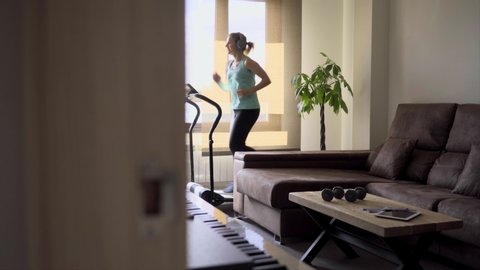 Beautiful caucasian blonde woman exercises on a treadmill in her living room. Healthy life concept.