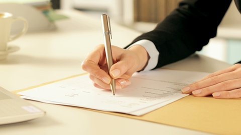 Close up of executive hands filling out form ticking checkboxes with a pen on a desk at office