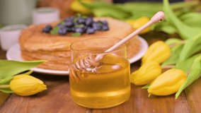 A wooden spoon with honey and a cup. Traditional pancakes with berries and honey on a wooden table. Spring breakfast and tulips.