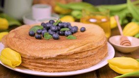 Pancake pancakes. Traditional Russian pancakes with blueberries and honey. A delicious spring breakfast and a bouquet of yellow tulips. 4K video