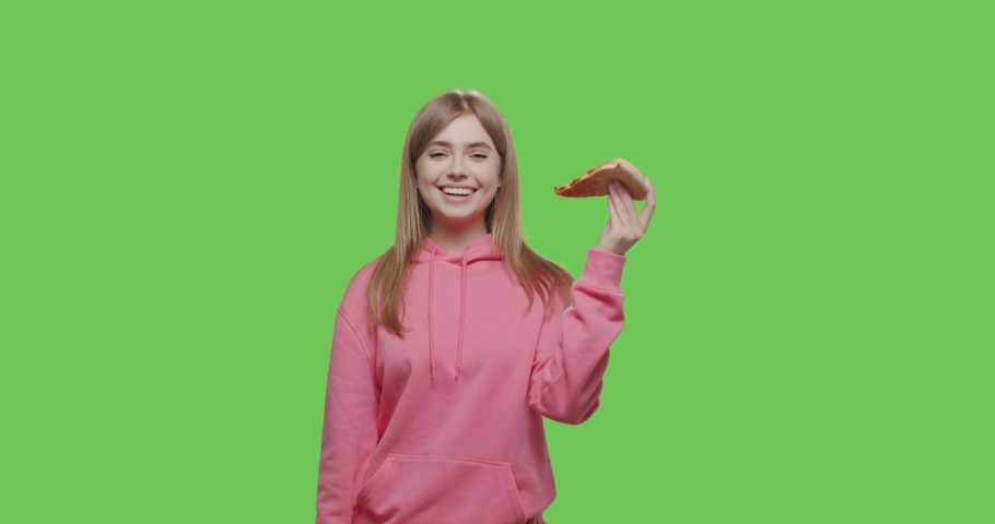 caucasian young woman eating slice of cheese vegetarian pizza for lunch on green screen. Girl taking piece of hot tasty italian fast food from hand over chroma key background. 4k raw footage
