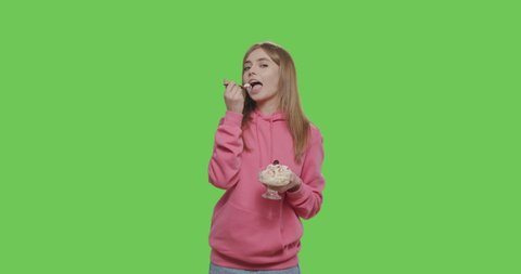 Young woman eating yogurt from glass vase at home on green screen. Long hair girl keeping spoon with ice cream over chroma key background.