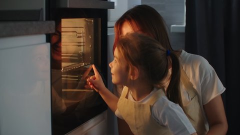Mother Mother and daughter watch as a pie is prepared in the oven. Happy childhood. Make homemade pizza together Stock Video