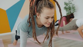 Smiling young lady with dreadlocks is exercising in yoga class with group of people wearing soirts clothing enjoying workout feeling carefree and relaxed. - Powered by Shutterstock - Get 15% off with code: PIKWIZARD15