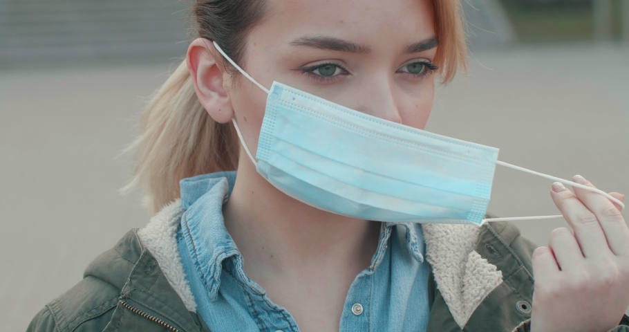 Closeup Face of young Woman wearing Protect Mask,looking directly to the Camera. Pandemic, portrait of a young tourist woman wearing protective mask on Street. N1H1 coronavirus, virus protection. Royalty-Free Stock Footage #1049122198