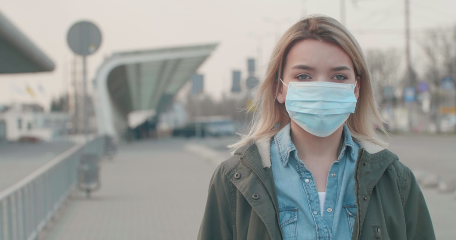 Young blonde Woman wearing a Protective Mask against infectious Diseases, walking near Bus Station. Pandemic Coronavirus2020. The concept health and safety, N1H1 coronavirus, virus protection. Royalty-Free Stock Footage #1049122336