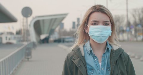 Young blonde Woman wearing a Protective Mask against infectious Diseases, walking near Bus Station. Pandemic Coronavirus2020. The concept health and safety, N1H1 coronavirus, virus protection.