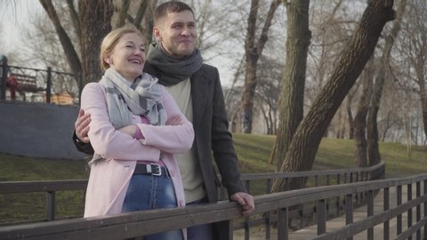 Laughing young man hugging older cheerful woman in park. Portrait of happy loving Caucasian couple with age difference dating outdoors on sunny autumn day. Love, romance, leisure, lifestyle.