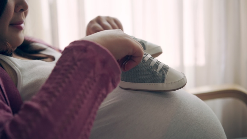 Pregnant woman feeling happy at home while taking care of her child. The young expecting mother holding baby in pregnant belly. Maternity prenatal care and woman pregnancy concept. Royalty-Free Stock Footage #1049130715