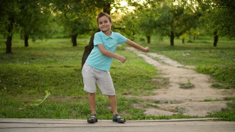 Smiling teenage boy dancing outside. Happy child making rhythmical movements in summer park. Cheerful boy having fun outdoor in slow motion.