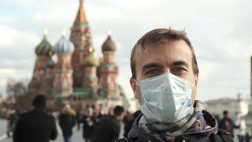 Disease outbreak, coronavirus covid-19 pandemic, air pollution in Moscow, Russia. Portrait of adult man with medical protective mask on face with Kremlin, Red square, people crowd on background. 