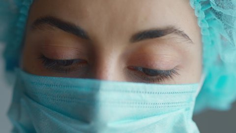 sad and tired medic opens eyes and looking atraight at camera. medical stuff portrait closeup. Woman in Protective Face Mask, 