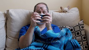 Young male in medical mask relaxing on sofa and playing online game on mobile phone while spending time during COVID quarantine at home