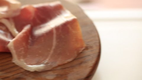 Thin slices of pork ham on the wood plate. Dolly shot. Closeup