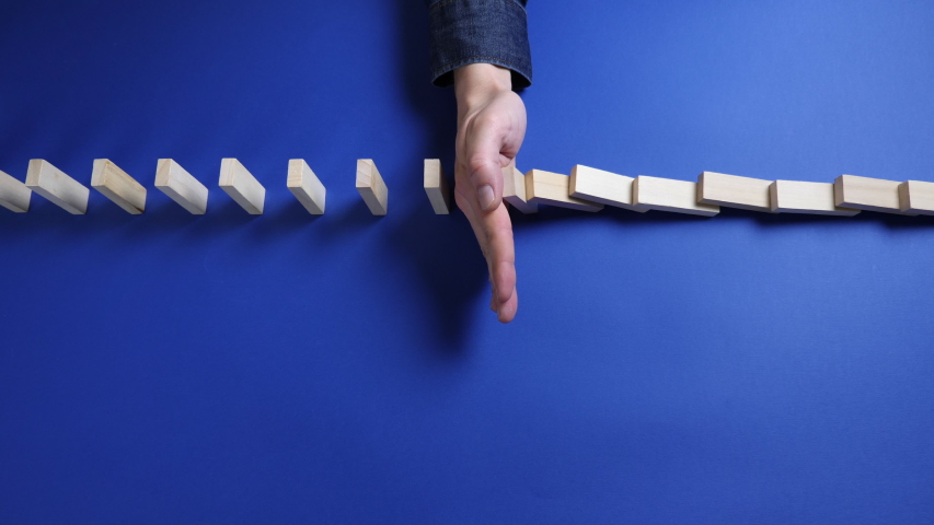 Top view: Close up hand of a businessman stopping falling blocks on blue background.