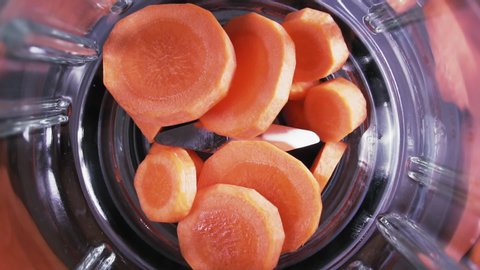 Carrot slices fall into blender, slow motion. Orange smoothie in blender, top view. Healthy eating concept.