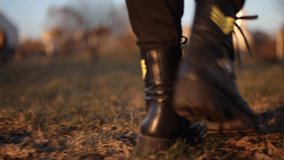 Video 4K female legs in black berets boots walk along the grass and along the track in the evening sunlight, golden hour is autumn or spring.