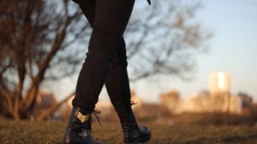Video female legs in black berets boots walk along the grass and along the track in the evening sunlight, golden hour is autumn or spring.