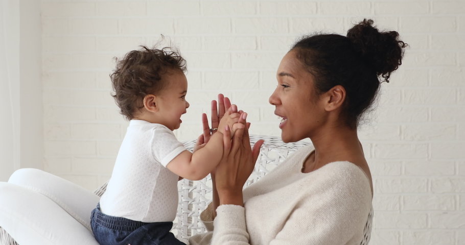 Adorable infant baby girl daughter playing patty cake with african mom at home. Happy mixed race family mother and cute little boy son learning funny game having fun enjoying sweet moments together. | Shutterstock HD Video #1049156386