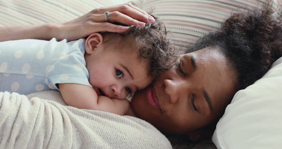 Loving african young mommy hugging soothing adorable sweet baby boy lying in bed. Smiling caring mixed race mother and cute little infant child girl cuddling in bedroom. Mum and child tender moments.