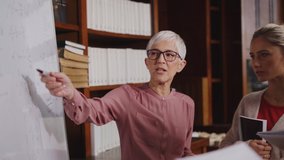 Professor helping student in library at college. Group of multiethnic students taking an active part in a lesson while standing in library. Mature woman teacher and university student discussing. - Powered by Shutterstock - Get 15% off with code: PIKWIZARD15