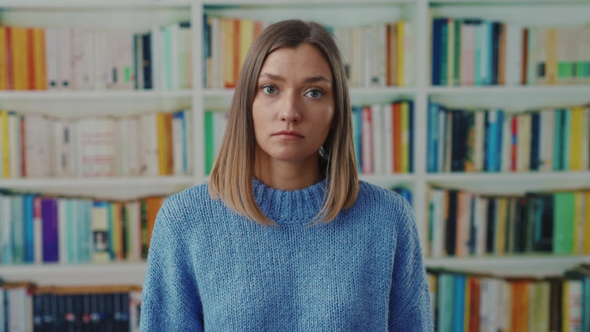 Academic pretty student woman shrugging her shoulders in hesitation shows helpless face cant help or dont understand. posing near bookshelves at library. Doubt, misunderstanding. Royalty-Free Stock Footage #1049159455