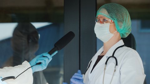 Doctor gives an interview to a reporter, both in protective suits