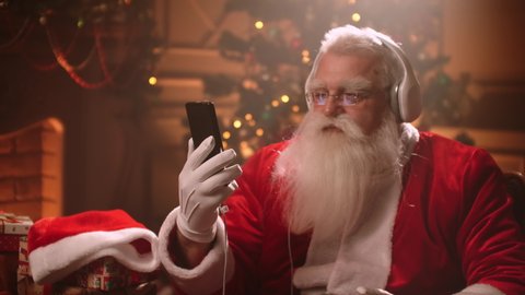 Santa Claus is having fun and relaxing listening to Christmas music in headphones