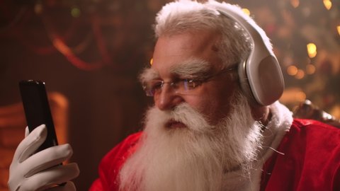 Santa Claus is having fun and relaxing listening to Christmas music in headphones