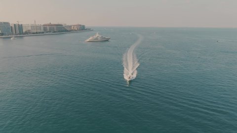 Aerial view of cruising motorboat and unknown anchored luxury motor yacht offshore in Dubai, UAE