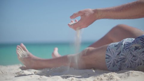 Guy Relaxing On Tropical Beach. Happy Calm Healthy Young Man Resting On Ocean. Hand Playing With Sand On Bahamas Vacation Holiday.Man Pouring Sand Through Fingers.Guy Sitting On Beach Caribbean Coast 