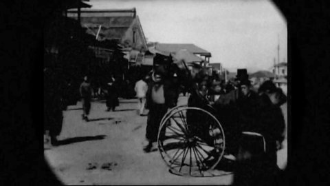 CIRCA 1897 - People walk and ride rickshaws down a road in Tokyo, Japan.