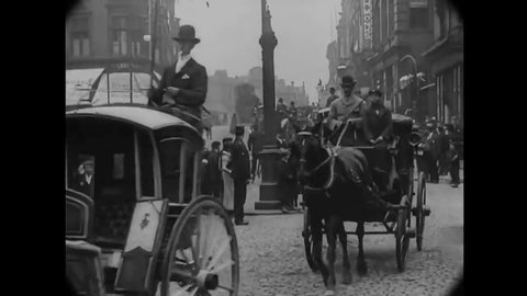 CIRCA 1902 - Horse-drawn carriages and coaches are driven down a busy English street.
