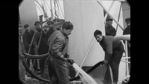 CIRCA 1900 - English sailors use a hose and brooms to clean the deck of a ship.