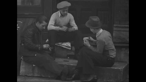 CIRCA 1930s - Men smoke and play cards on a Chicago stoop and boys congregate outside a row of slum houses during the Great Depression in America.