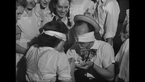 CIRCA 1940s - A blindfolded man and woman feed each other to the amusement of a crowd at a rec center, while women outdoors do a synchronized dive.