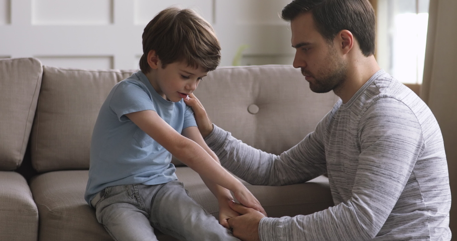 Young father holding hand, stroking shoulder of little child son, asking for forgiveness, apologizing at home. Compassionate dad helping small kid boy coping with bullying, sincerely talking indoors. Royalty-Free Stock Footage #1049193892
