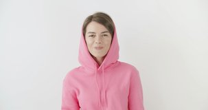  girl dressed in pink hoodie standing over white background blowing bubblegum candy bubbles and chewing gum. Woman looking at camera. 4k raw video footage slow motion