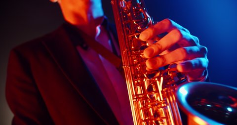 Cool saxophone player performing a solo on stage, spotted by red and blue light. Musician playing in jazz band - close up 4k footage