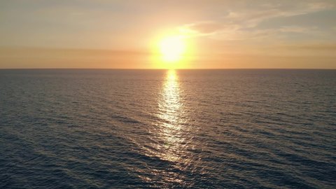 AERIAL: Golden reflections on sea water surface at sunset, aerial video, drone point of view, drone flying above sea surface. Sea surface with reflections of sunset. Drone flying from left to right