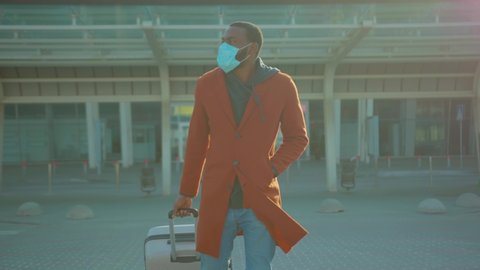 African American man wearing Protective Face Mask to avoid disease COVID-19 coronavirus infection with suitcase near airport pandemic disease virus male tourist epidemic air health illness slow motion