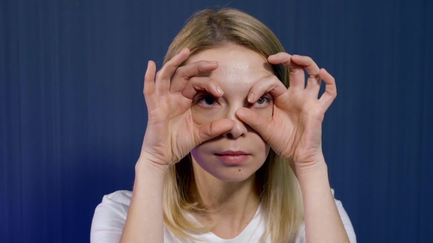 Close-up portrait of a young blonde girl who is in the Studio on a blue background, she is engaged in facial massage and facial gymnastics. Creates an area around the eyes.