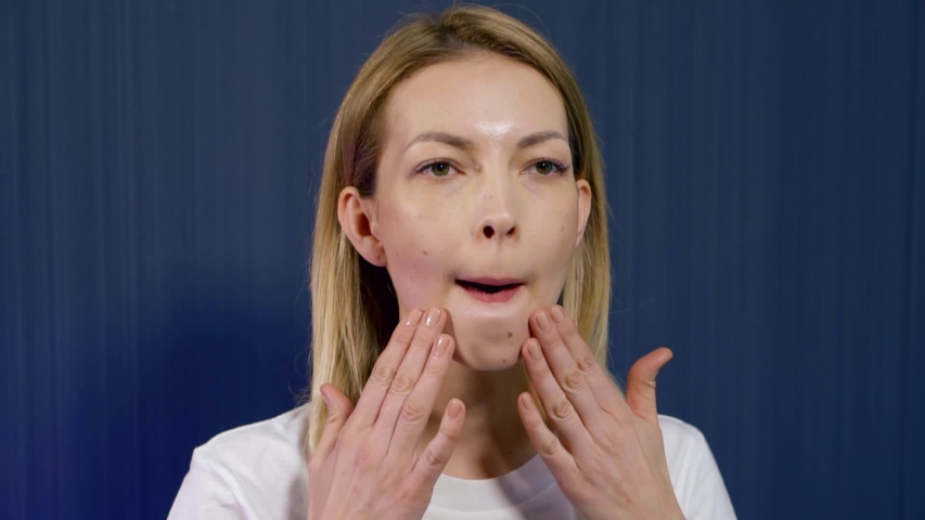 Close-up portrait of a young blonde girl who is in the Studio on a blue background, she is engaged in facial massage and facial gymnastics . Makes the chin area.