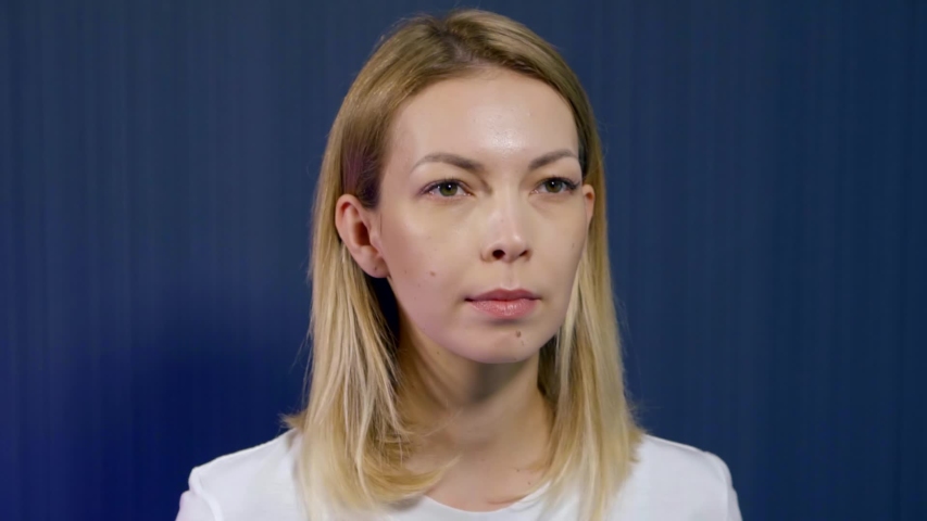 portrait of a young blonde girl who is in the Studio on a blue background, she is engaged in facial massage and facial gymnastics. Makes an area of the cheeks with a cork in the mouth.