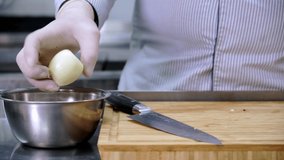 Chef takes gloved peeled onion from metal bowl and cuts it into thin slices with knife on wooden bamboo Board in kitchen restaurant. Dolly sliding video