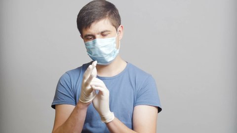 young doctor in surgical mask on a gray studio background, concept of medicine and health, medical worker getting ready for surgery putting on sterile latex gloves