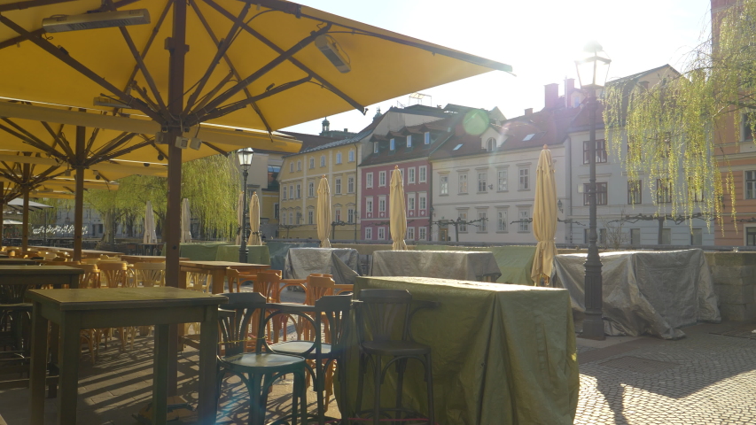 LENS FLARE: Golden spring sunbeams shine on terrace of a restaurant, closed as a result of a coronavirus quarantine. Riverside bars and restaurants in Ljubljana are closed due to covid-19 epidemic. Royalty-Free Stock Footage #1049230420