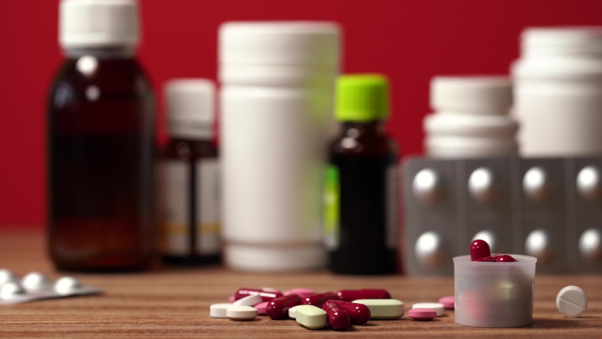 Closeup view 4k video of throwing pair of white latex gloves on brown wooden table full of different tablets, drugs, vitamins and bottles.